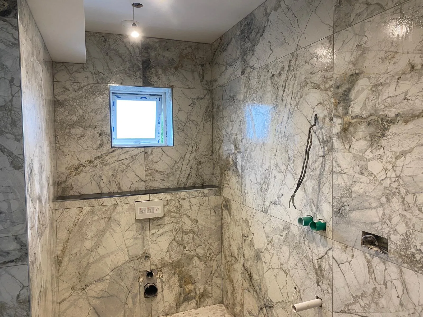 Shower enclosure lined in large-format white and grey marble-effect porcelain with book-matched veining and a slim stone shelf