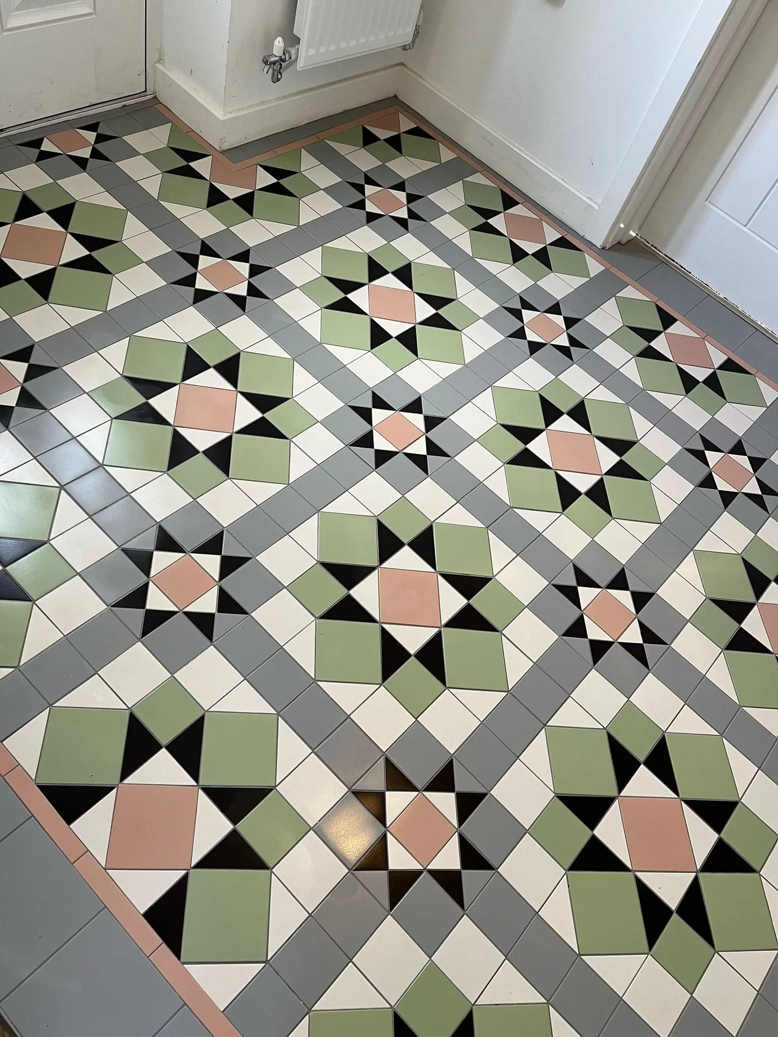 Geometric floor tiles in sage-green, salmon-pink, black and cream laid on the diagonal, with wide grey banding and a salmon-pink border line