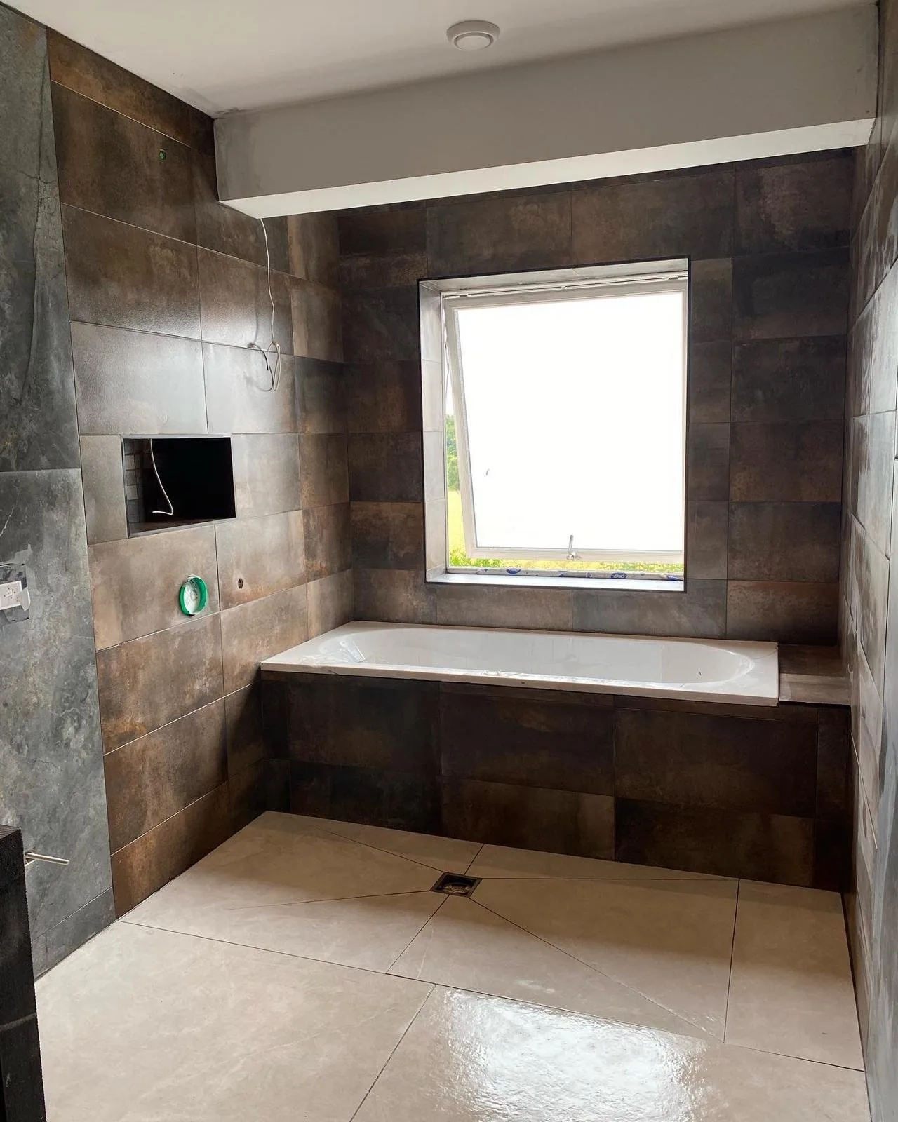 Bathroom mid-fit in bronze metallic-effect tiles, the floor tiles cut on the diagonal around a square wet room gully