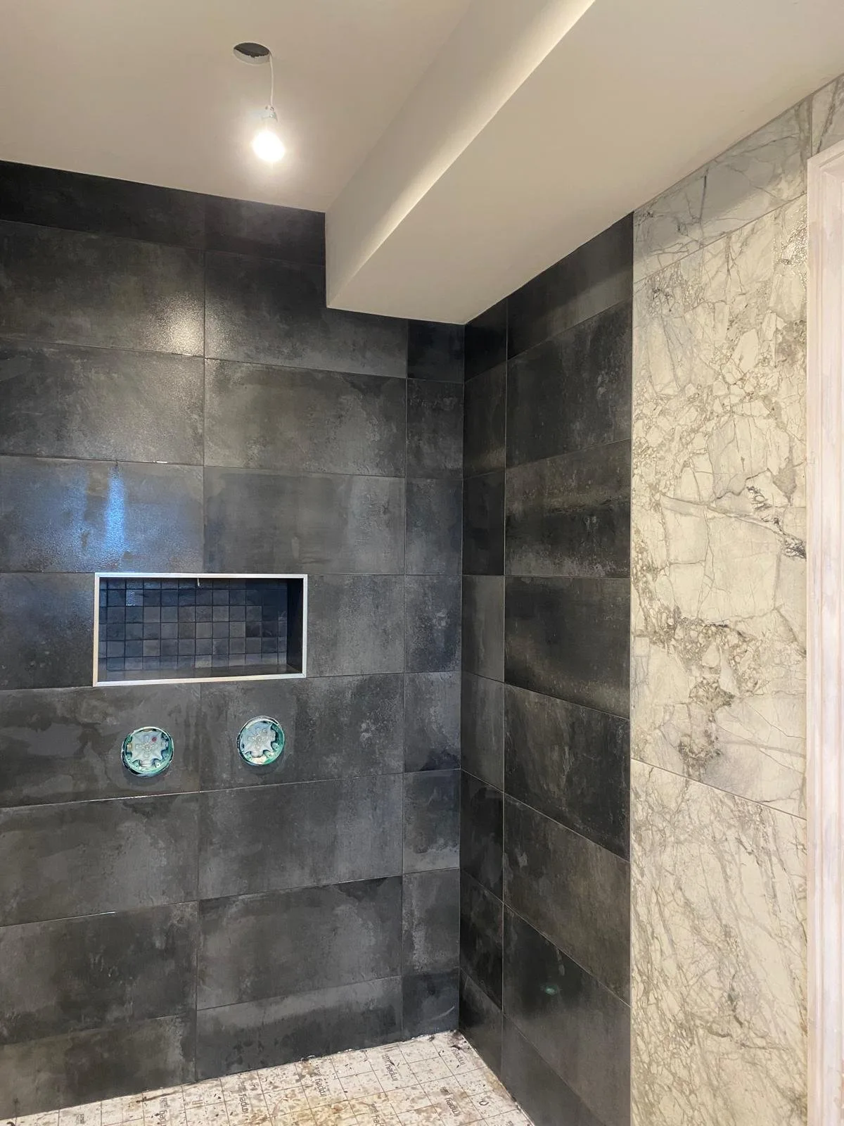 Walk-in shower mid-fit in dark grey concrete-effect large-format tiles, beside a book-matched marble-veined feature wall