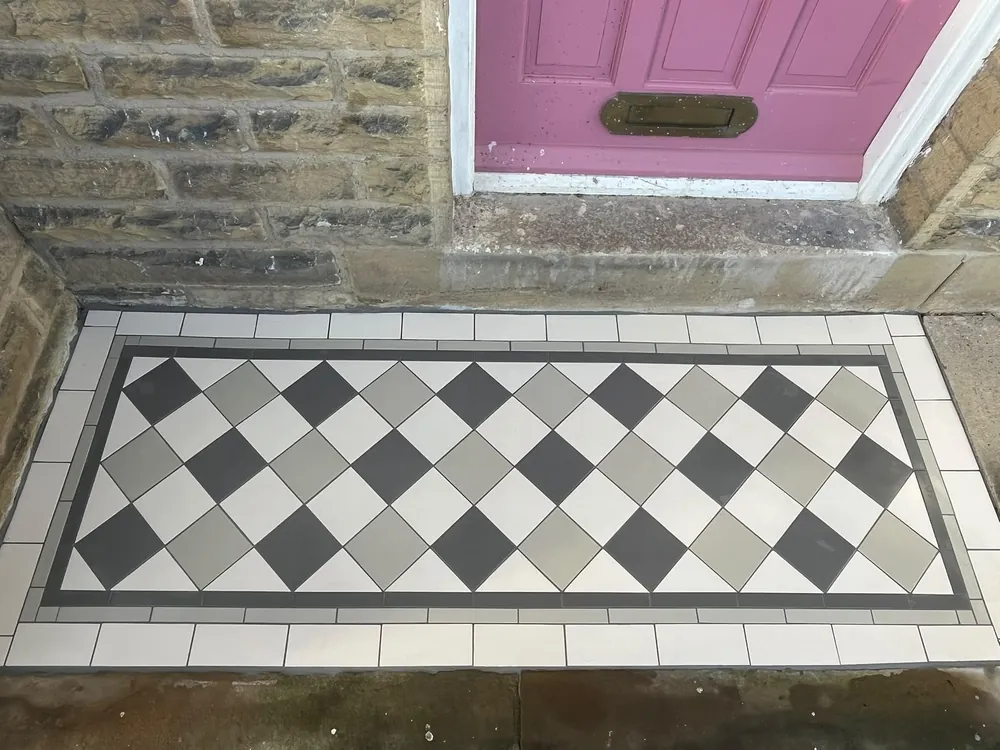 Charcoal, mid-grey and white tiles laid diagonally in a diamond pattern with a dark grey border, forming an entrance panel at the foot of a stone step