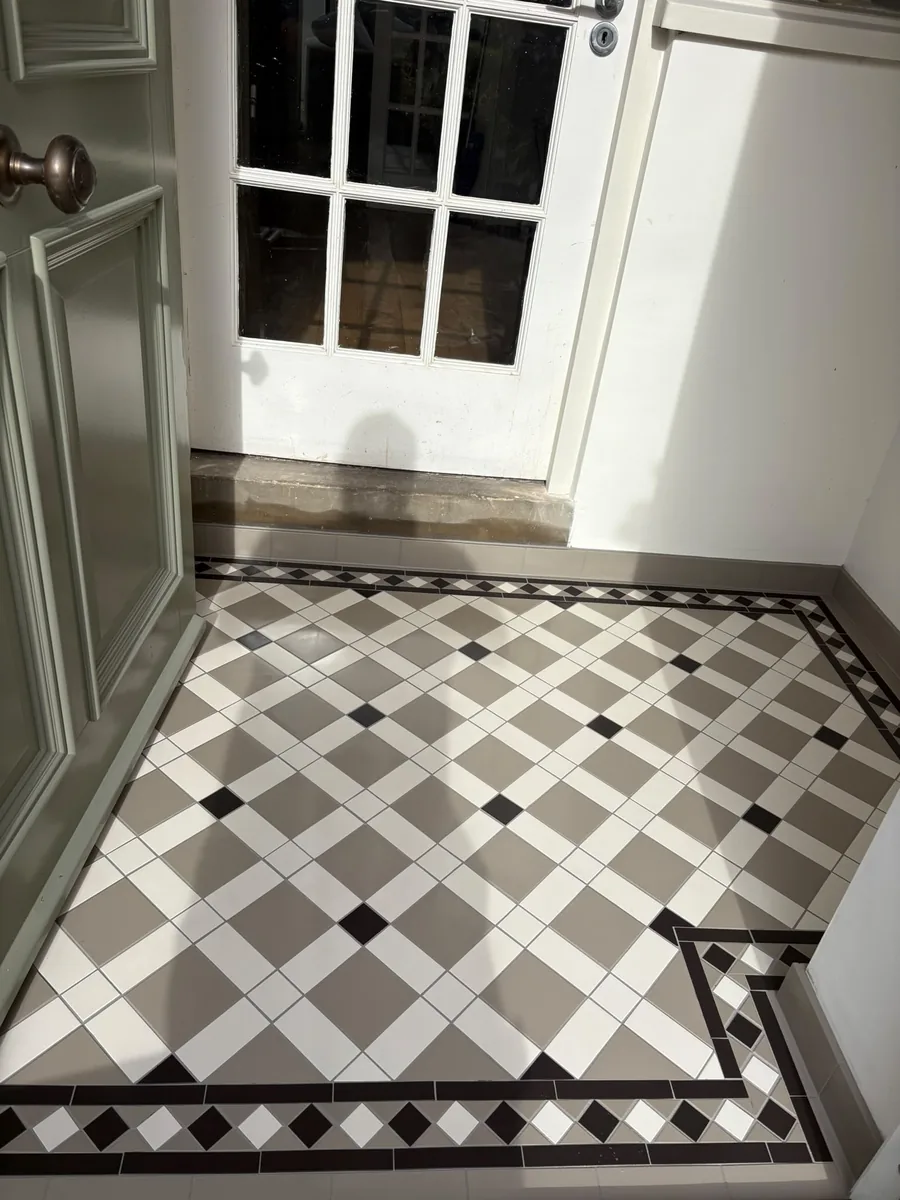 Grey and white lattice floor with small black square insets and a black-and-white diamond border, between an open sage-green panelled door and a white glazed door, with grey tiled skirting
