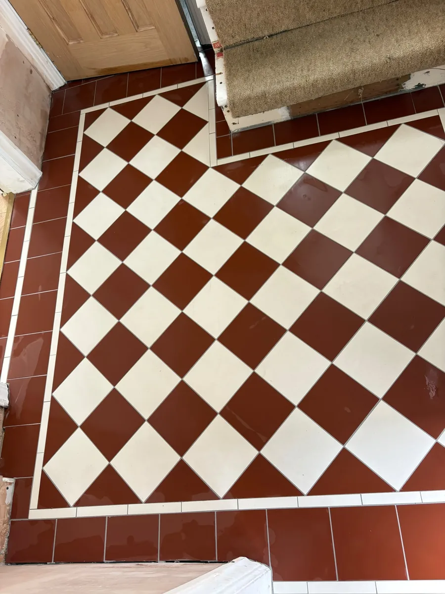 Red and white tiles laid on the diagonal in a chequerboard, edged with a narrow white strip and a border of plain red tiles, the pattern stepping around the foot of a carpeted staircase