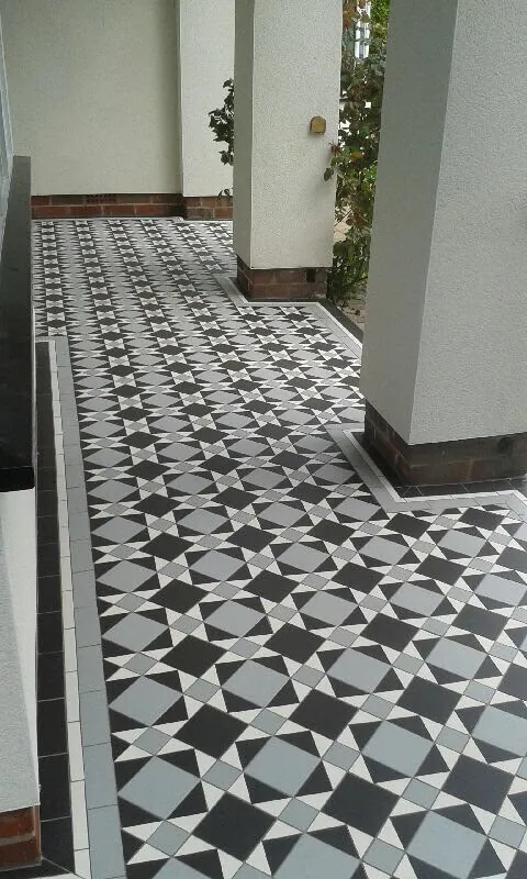 Geometric porch floor in dark charcoal, pale grey and off-white laid in a four-point star pattern, turning the corner around a rendered pillar