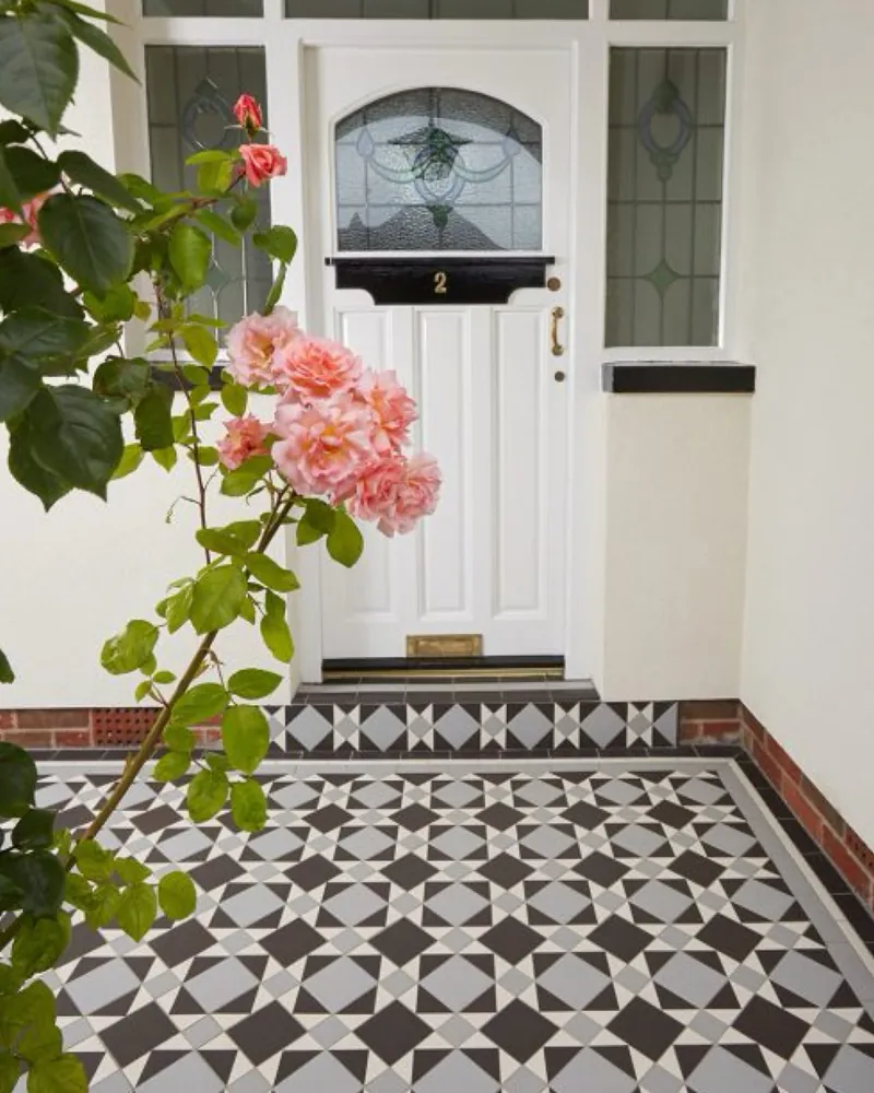 Geometric porch floor in dark charcoal-brown, pale grey and off-white in a four-point star pattern, at a white panelled front door with leaded glass